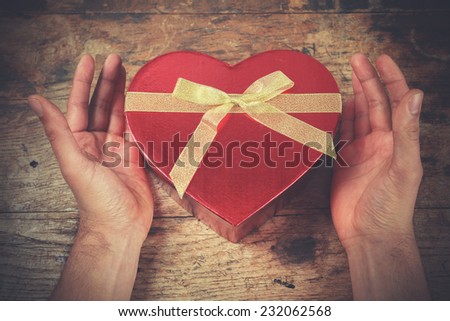 A man\'s hands are resting on a wooden surface with a heart shaped box
