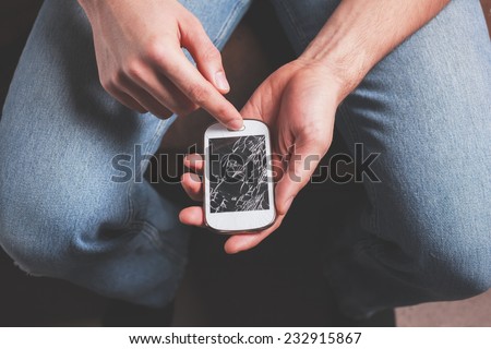 A young man is sitting holding a broken smart phone