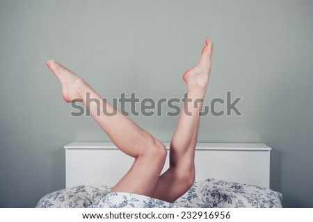 A young woman is lying in bed with her naked legs raised
