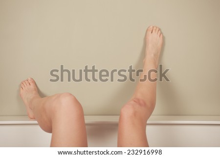 A young woman is lying in bed with her naked legs raised