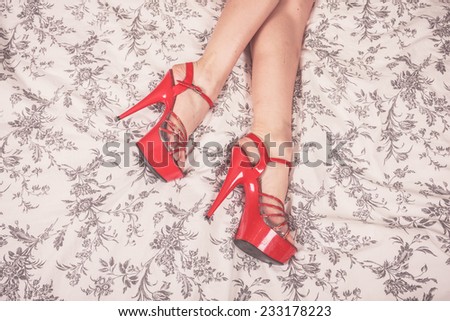 A young woman is lying on a bed and is wearing red stripper heels