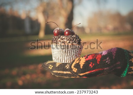 A gloved hand is holding a cupcake with a cherry on top
