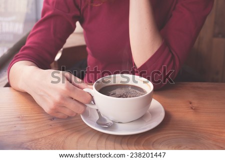 A young woman is having a cup of coffee by the window in a cafe