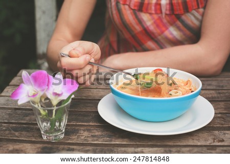A young woman is eating tom yum soup at a table outside