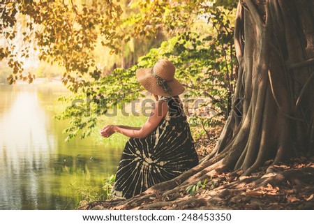 A young woman is sitting under a tree by the river