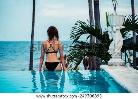 A young woman is sitting by the edge of an infinity pool by the ocean