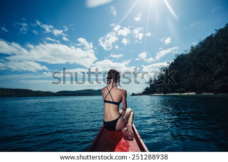 A sexy young woman wearing a bikini is sitting on a small boat near a tropical island