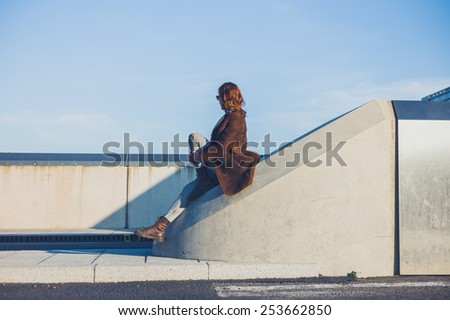 A young woman is sitting on a concrete barrier in the middle of a road in the winter