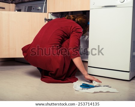 A young woman is trysing to fix the plumbing under the kitchen sink