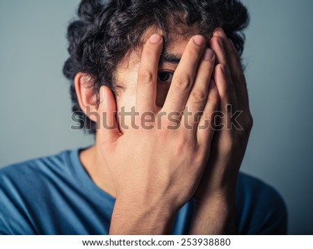 A scared young man is covering his face and is looking though his fingers