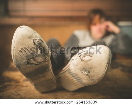 A young woman wearing worn out shoes is resting her feet on a table at home