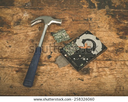 A hammer and a smashed computer harddrive on a wooden surface