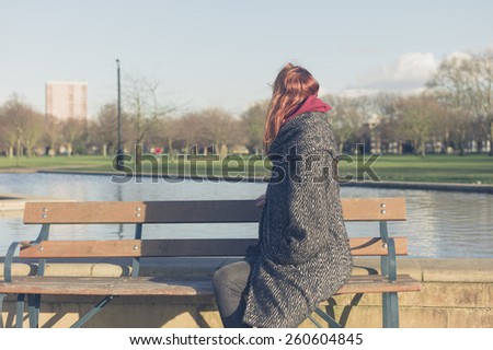 A young woman is relaxing on a bench by water feature in a park
