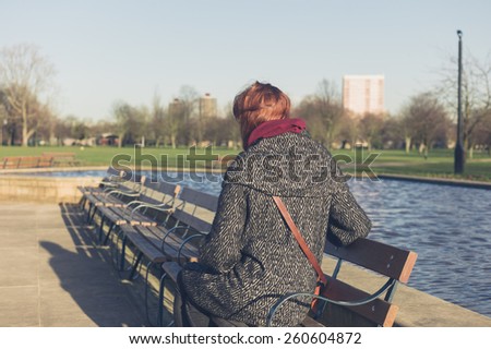 A young woman is relaxing on a bench by water feature in a park