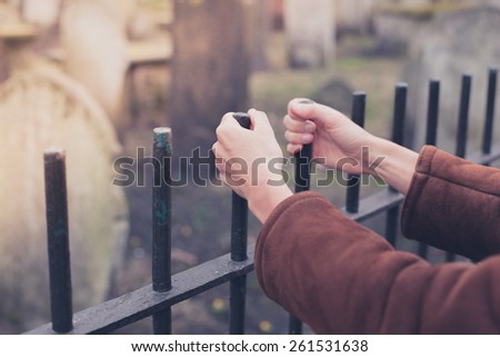 A pair of hands are holding a fence surrounding a graveyard
