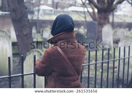 A woman is standing by a fence and is looking at some graves in a cemetery