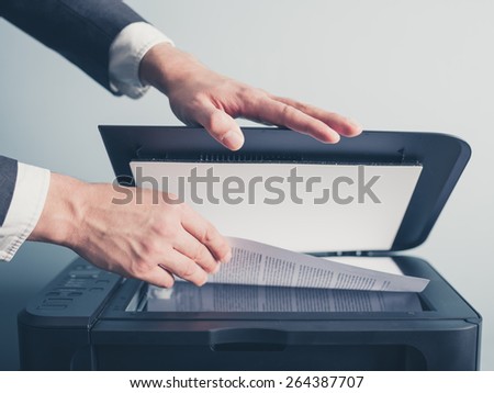 The hands of a young businessman is placing a document on a flatbed scanner in preparation for copying it