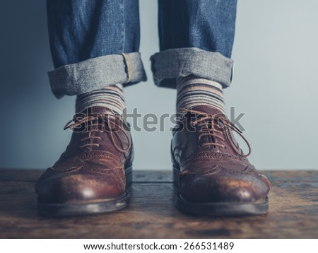 The feet of a man standing on a wooden floors wearing stripey socks and leather shoes