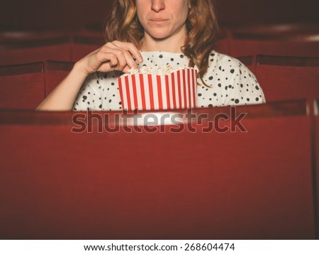 A young woman is watching a movie and is eating popcorn at the cinema