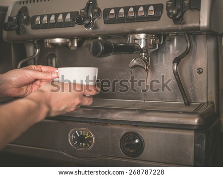 The hands of a young woman is placing a cup under the dispenser of a professional coffee machine