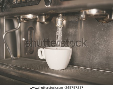 Professional coffee machine with a small white cup getting water dispensed into it