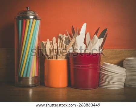 A selection of cutlery, colorful straws and plastic lids for disposable cups on a wooden table