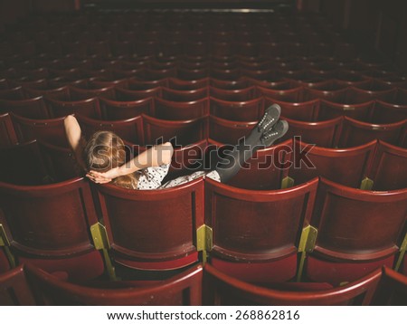 A young woman is sitting in an auditorium with her feet on the seats in front