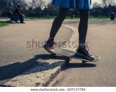 A young woman is performing a skateboard trick on the curb in a park