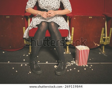 A young woman is sitting in a movie theater with popcorn on the floor