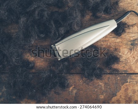 Hair clippers on a wooden surface surrounded by piles of cut hair