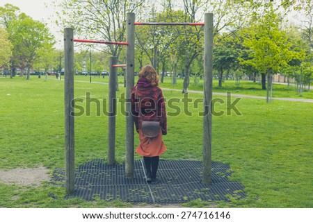 A young woman is standing in a park by some pull up bars
