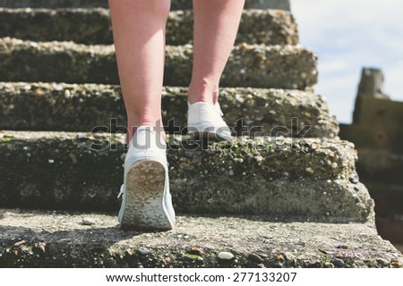 The legs and feet of a young woman as she is walking up some step by the sea