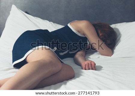A young woman wearing an elegant blue dress is sleeping on a bed