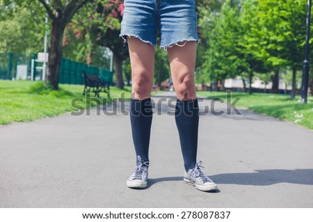 A young woman wearing knee high socks is standing in a park on a summer day