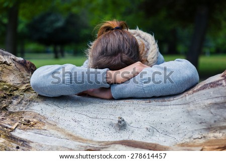 A sad young woman is resting her head on a tree trunk in the park