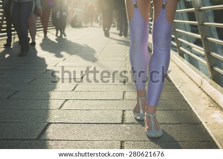 A young woman wearing heels and sexy leggings is walking on a pedestrian bridge in the city