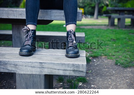 A young woman wearing boots is sitting on a bench in a park