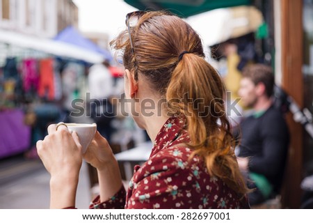 A young woman is having a cup of coffee outside at a table on the street