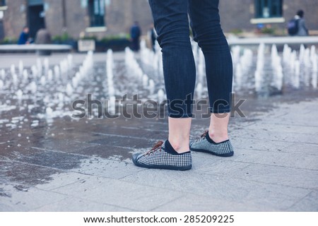 The legs of a young woman as she is standing by a small fountain in the city