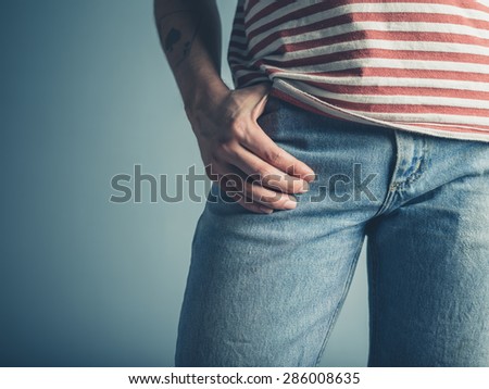 A sexy young man is posing with one hand in his pocket