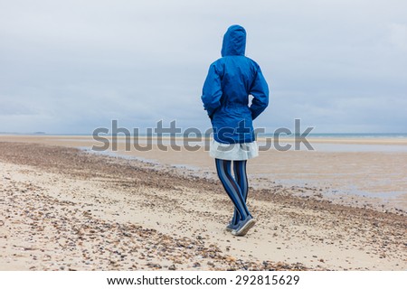 A young woman wearing a blue waterproof jacket is walking on the beach on a cold day