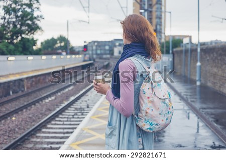A young woman is standing on a platform with a cup of coffee and is waiting for the train