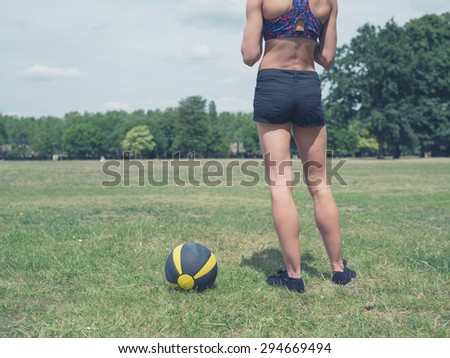 Vintage toned shot of a fit and athletic woman is standing in the park with a medicine ball on a sunny summer day