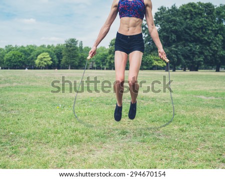 A fit and athletic young woman is skipping with a jump rope in the park on a summer day