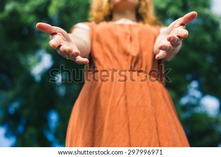 A young woman is standing in nature and is offering her hands to help