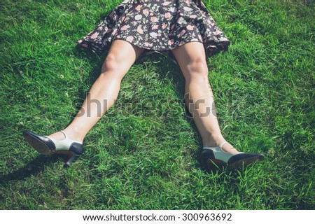 The legs of a young woman wearing a dress as she is lying on the grass in a field