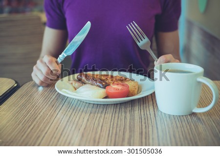 A young woman is sitting at a table in a cafe about to enjoy a traditional english breakfast