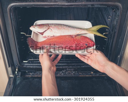A pair of hands are placing a tray with two exotic fish in the oven