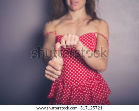 A young woman wearing a pretty dress is holding a hairband on her thumb and is pulling it back to shoot it
