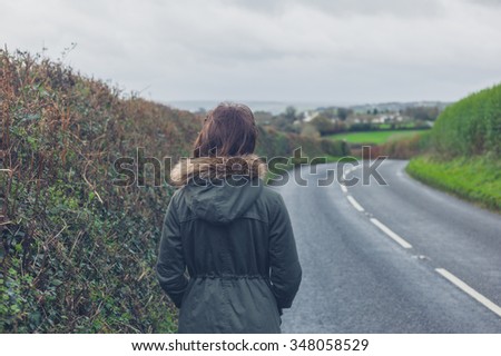 Rear view shot of a young woman walking on a country road by herself in the autumn or winter